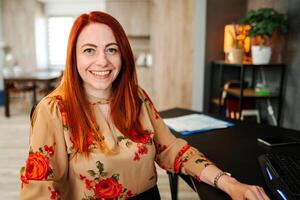 Portrait of a smiling red-haired woman at a desk photo