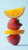 A stack of strawberry and orange slice fruit balancing on top with solid background photo