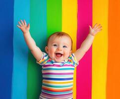 Cheerful toddler with arms raised against vibrant rainbow stripes photo