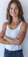 Smiling woman in a white tank top poses confidently against a light wall photo