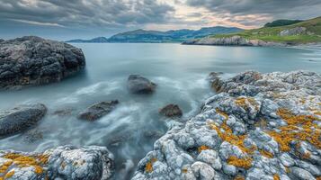 Ocean waves crashing on rocks with dramatic sky and cliffs in background photo