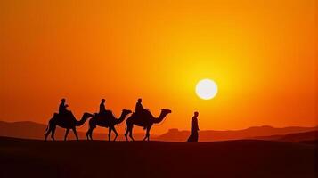 Silhouette of Camel Riders Against an Orange Hued Sky on a Desert Dunes Under Dramatic Sunset photo