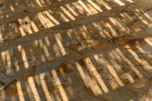 Natural stone wall texture with shadow flat lay. Top view of tropical summer background with leaf shade pattern. photo