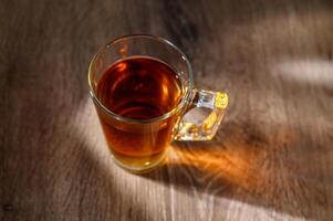 A clear glass cup of tea infused steaming on a wooden table photo