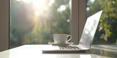 Blurred background of a modern home office interior with a laptop computer and a coffee cup on a white table, with copy space for text in the blurred window view. Business work from home concep photo