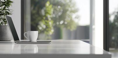 Blurred background of a modern home office interior with a laptop computer and a coffee cup on a white table, with copy space for text in the blurred window view. Business work from home concep photo
