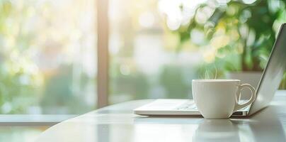 Blurred background of a modern home office interior with a laptop computer and a coffee cup on a white table, with copy space for text in the blurred window view. Business work from home concep photo