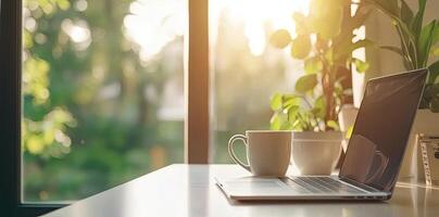 Blurred background of a modern home office interior with a laptop computer and a coffee cup on a white table, with copy space for text in the blurred window view. Business work from home concep photo