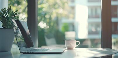 Blurred background of a modern home office interior with a laptop computer and a coffee cup on a white table, with copy space for text in the blurred window view. Business work from home concep photo