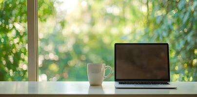 Blurred background of a modern home office interior with a laptop computer and a coffee cup on a white table, with copy space for text in the blurred window view. Business work from home concep photo