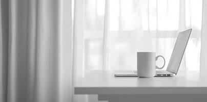 Minimalist white office desk with laptop and coffee mug on a blurred background, with space for text, representing the concept of working from home photo