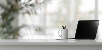 Minimalist white office desk with laptop and coffee mug on a blurred background, with space for text, representing the concept of working from home photo