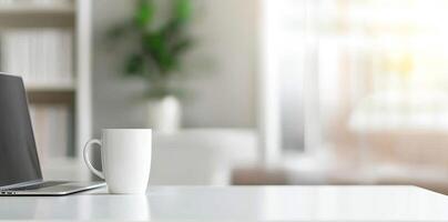 Minimalist white office desk with laptop and coffee mug on a blurred background, with space for text, representing the concept of working from home photo