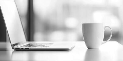 Minimalist white office desk with laptop and coffee mug on a blurred background, with space for text, representing the concept of working from home photo