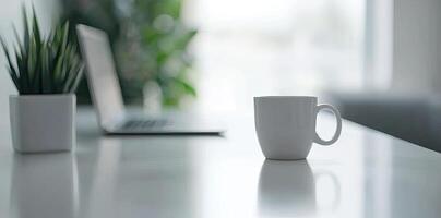 Minimalist white office desk with laptop and coffee mug on a blurred background, with space for text, representing the concept of working from home photo