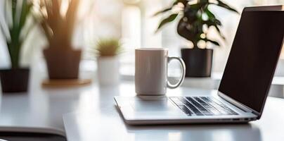 Minimalist white office desk with laptop and coffee mug on a blurred background, with space for text, representing the concept of working from home photo