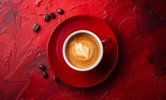 A red coffee cup with a white rim and a white swirl on top of it. The coffee is poured into the cup and there are coffee beans on the table photo