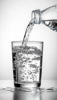 A glass of water is being poured into it. The water is clear and the glass is half full photo