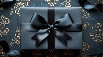 A black box with a bow on top of it. The box is placed on a table with a gold and black patterned cloth photo