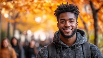 A man with a black hoodie and backpack is smiling for the camera. The scene takes place in a city street with people walking around. The man's smile suggests that he is happy and enjoying his day photo