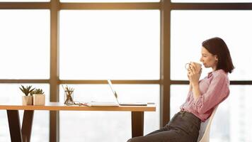 Watching Tutorial. Side view portrait of happy casual girl sitting at table, drinking hot coffee and using laptop photo