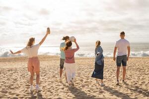 A group of five friends gathers on a sandy beach, having fun and laughing while tossing a volleyball under the sun. The ocean waves crash gently in the background. photo