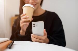 Close-up of a woman enjoying coffee while reading text on her phone at a table indoors or in a cafe. photo