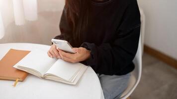 A close-up of a woman in a cozy sweater using her smartphone while reading at a table indoors. photo