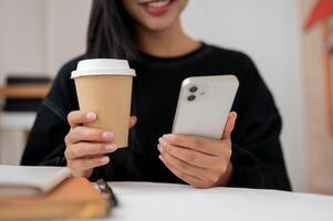 Close-up of a woman enjoying coffee while reading text on her phone at a table indoors or in a cafe. photo