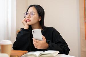 A thoughtful Asian woman gazes out the window while sitting at an indoor table, deep in thought. photo