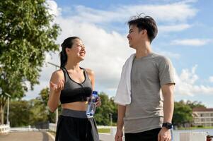 A happy Asian couple is enjoying a conversation while walking together after a jog in a park. photo