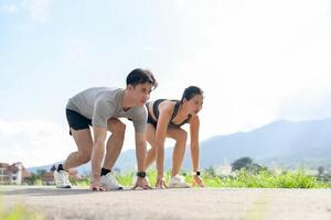 A confident, sporty Asian couple in sportswear is getting ready to sprint in the park. photo