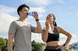 A tired, sweaty couple in sportswear is resting together after a long run in a park on a sunny day. photo