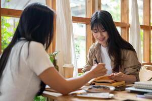 Two cheerful Asian college students are doing their homework and reading together in a coffee shop. photo