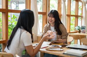 Two cheerful Asian college students are enjoying talking and reading together in a coffee shop. photo