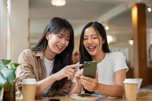 Two female friends are looking at something on a smartphone, laughing, and enjoying a conversation. photo