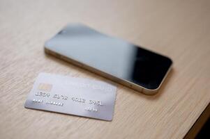 A close-up of a credit card and a smartphone placed on a wooden table indoors. photo