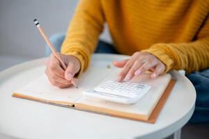A woman writing in a book and using a calculator to manage her household expenses. photo