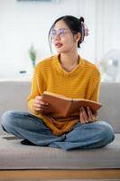 A beautiful Asian woman is daydreaming while looking out the window and enjoying reading a book. photo