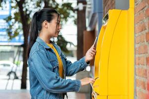 A side view of a beautiful Asian woman inserting her debit card into an ATM to withdraw some money. photo