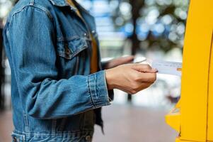 A close-up of a woman in a denim jacket inserting her debit card into an ATM to withdraw some money. photo