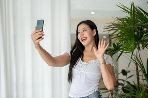 A charming Asian woman is enjoying talking on a call while standing by a window indoors. photo