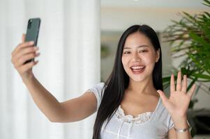 A charming Asian woman is enjoying talking on a call while standing by a window indoors. photo
