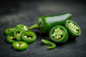 Fresh jalapeno peppers cut and arranged on a dark textured background showing vibrant green color and seeds photo