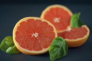 Freshly cut grapefruit slices on a dark surface surrounded by vibrant green basil leaves photo