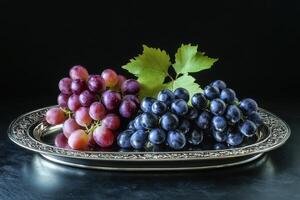 Fresh red and blue grapes arranged on an ornate silver platter against a dark background photo