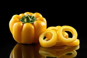 Yellow bell pepper and sliced rings displayed on a black reflective surface in a creative food setting photo