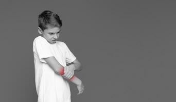 The youngster's face contorted in pain as he touches his elbow, suggesting an injury isolated on grey photo