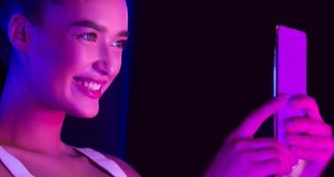 A woman is smiling while holding a cell phone in her hand. She is looking directly at the camera with a happy expression on her face. photo