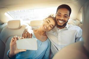 A happy black couple is taking a selfie in the backseat of a car. The woman is leaning on the mans shoulder while he holds her hand and smiles. The image captures the joy and intimacy photo